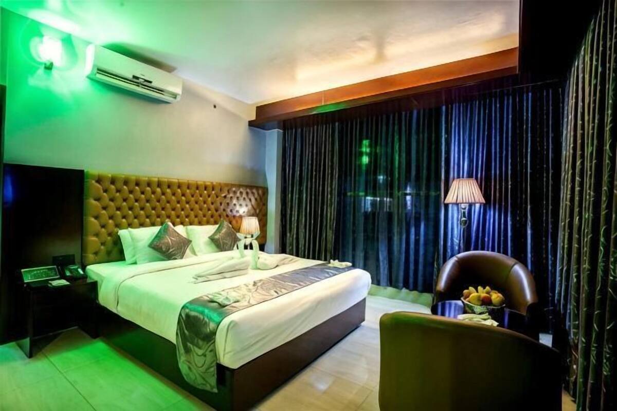 Quarto de hotel com uma cama grande, uma mesa de cabeceira com abajur, uma cadeira e vista para o exterior pela janela.