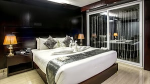 A hotel room with a large bed, a nightstand with a lamp, a telephone, and a view through a glass door. - Momo Inn (Bogra)