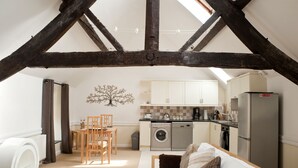 A compact kitchen with modern appliances, a dining area with a wooden table and chairs, and a cozy seating area with a sofa and cushions. - Bryn Melyn Farm Cottages- 5 Luxury Cottages In A Stunning Setting with Wood Fired Hot Tub (Bala)