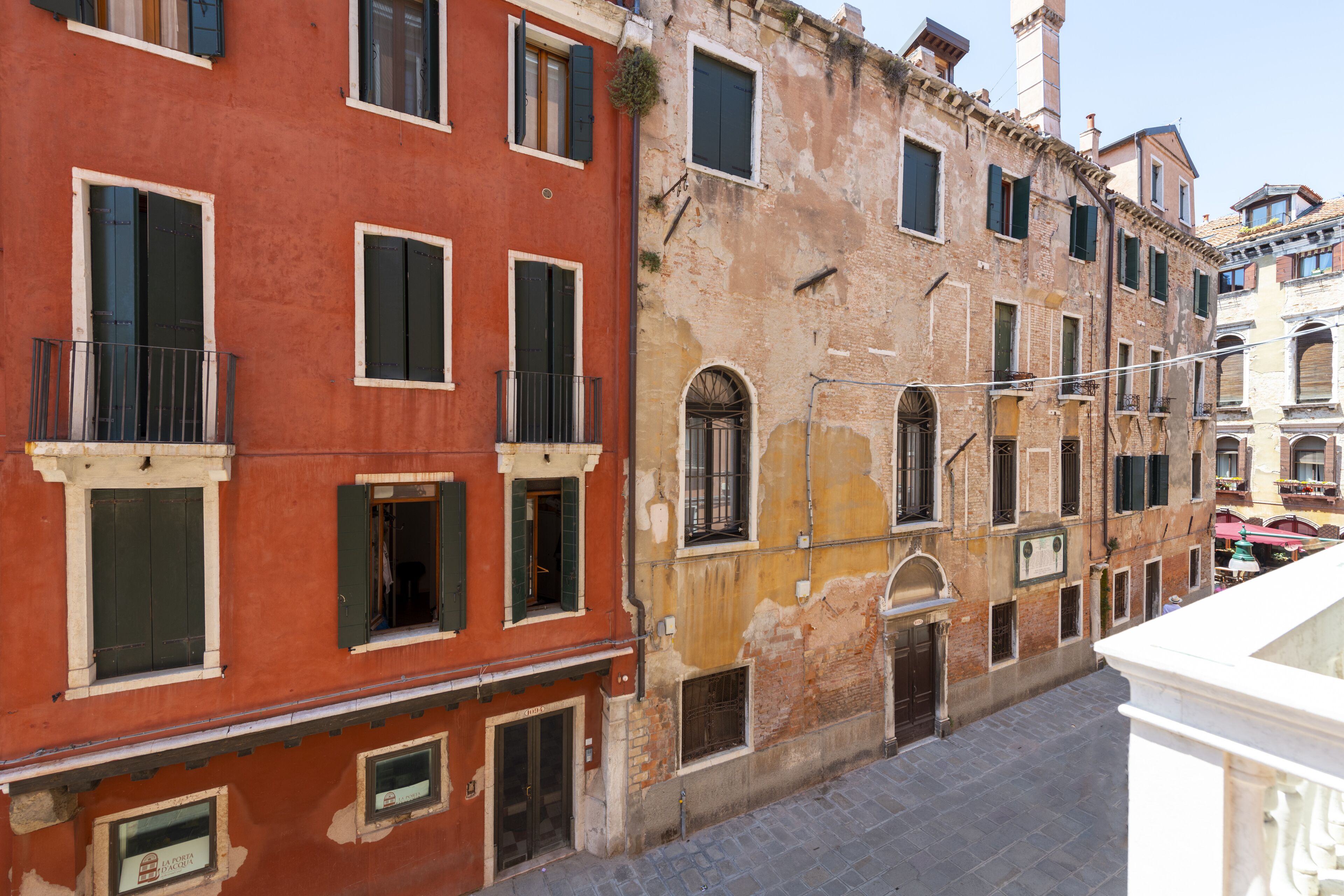 A narrow street with historic buildings, including a red building with balconies and a yellow building with arched windows.