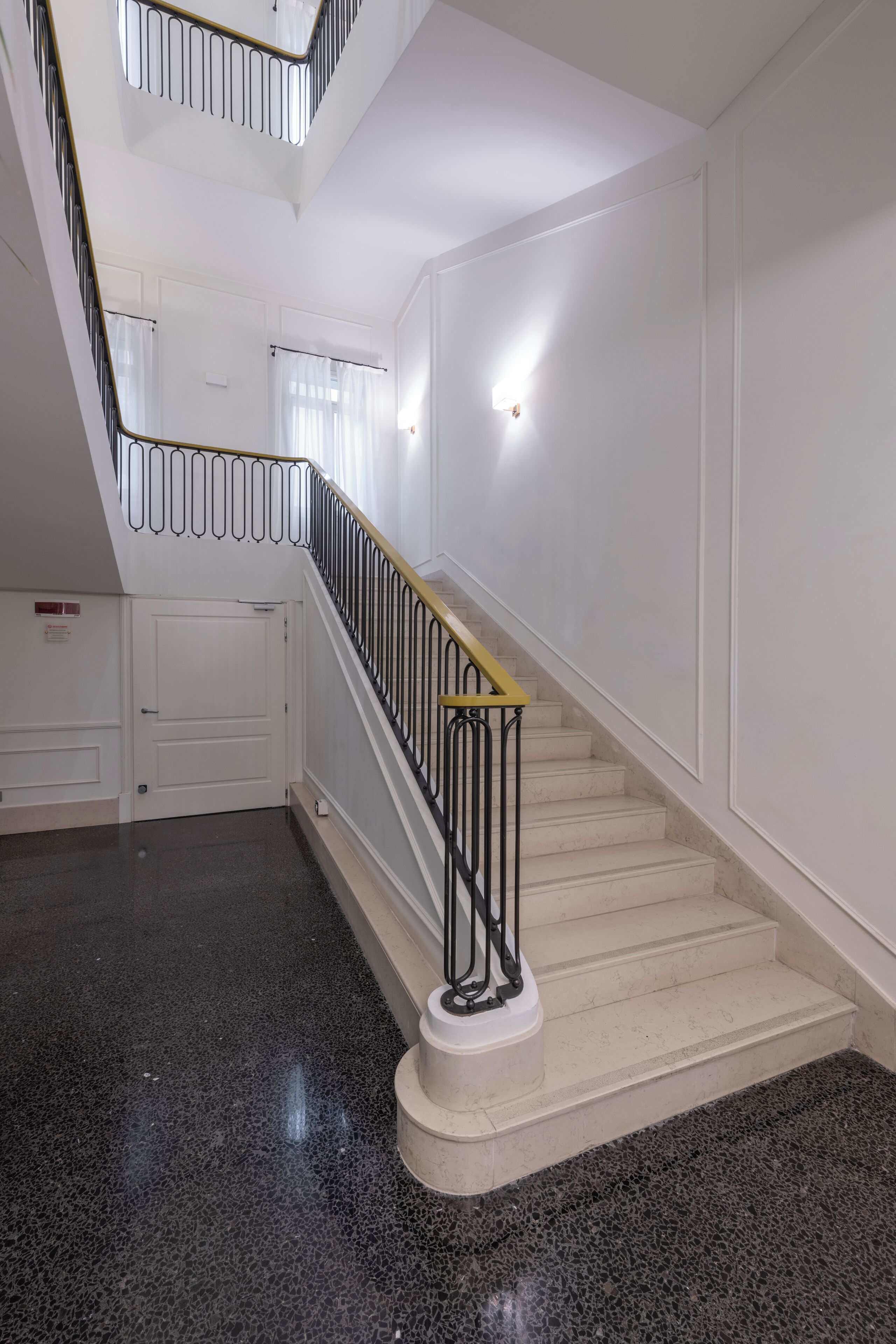 A staircase with a black and gold handrail, white walls, and a dark speckled floor.