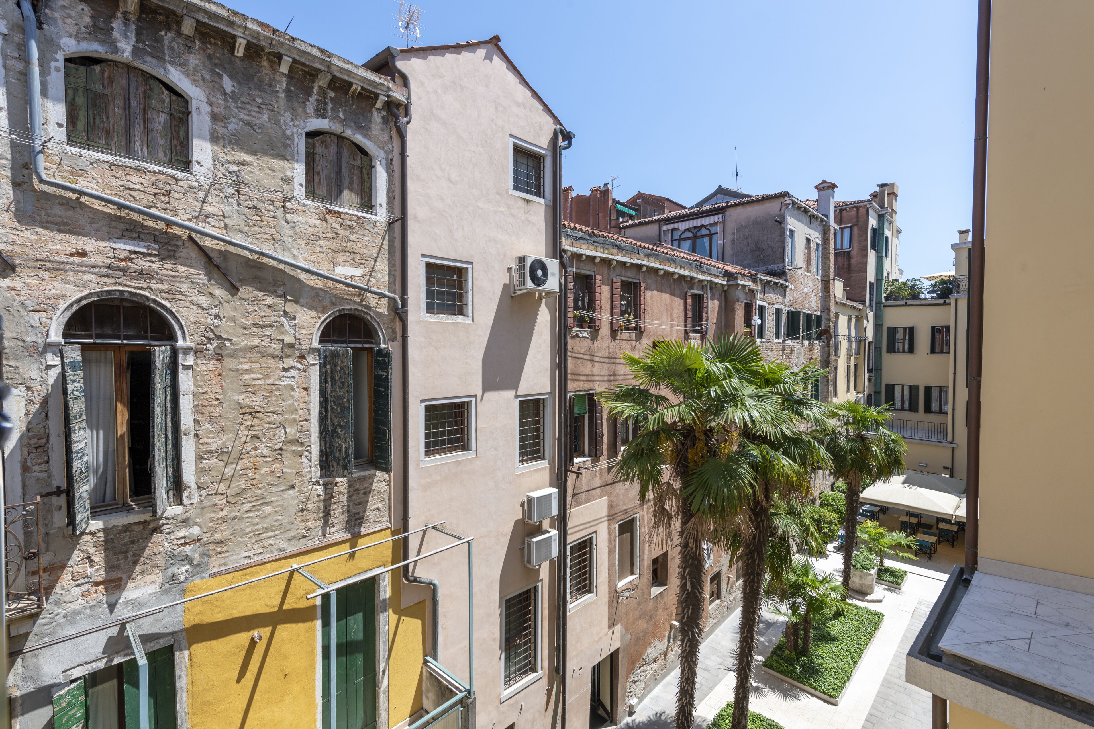 A narrow street with historic buildings, including a stone building with arched windows and a yellow facade.