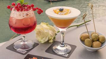 Une table avec un verre à martini, un cocktail aux fruits rouges, une rose et deux amuse-gueule sur une ardoise noire.