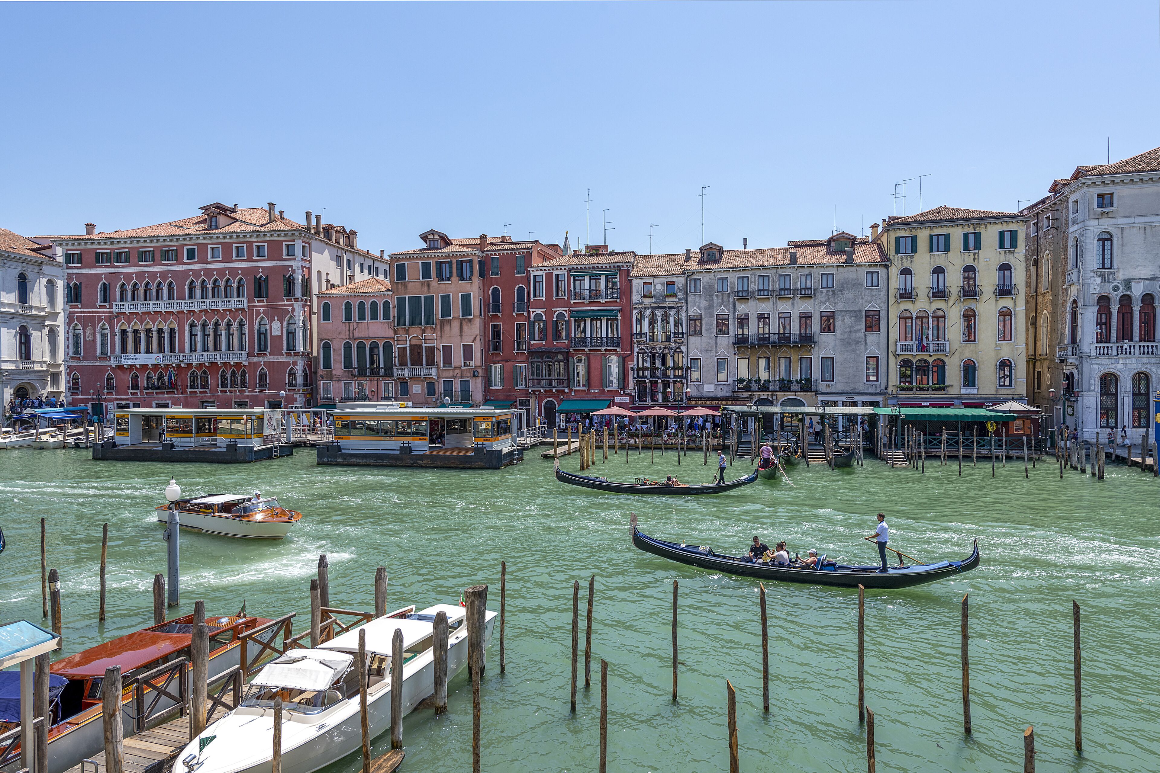 A canal with gondolas and boats, surrounded by historic buildings with varied architecture.