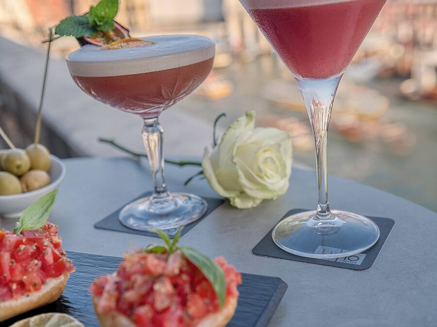 Duas taças de martini sobre uma mesa, com um panorama urbano ao fundo.