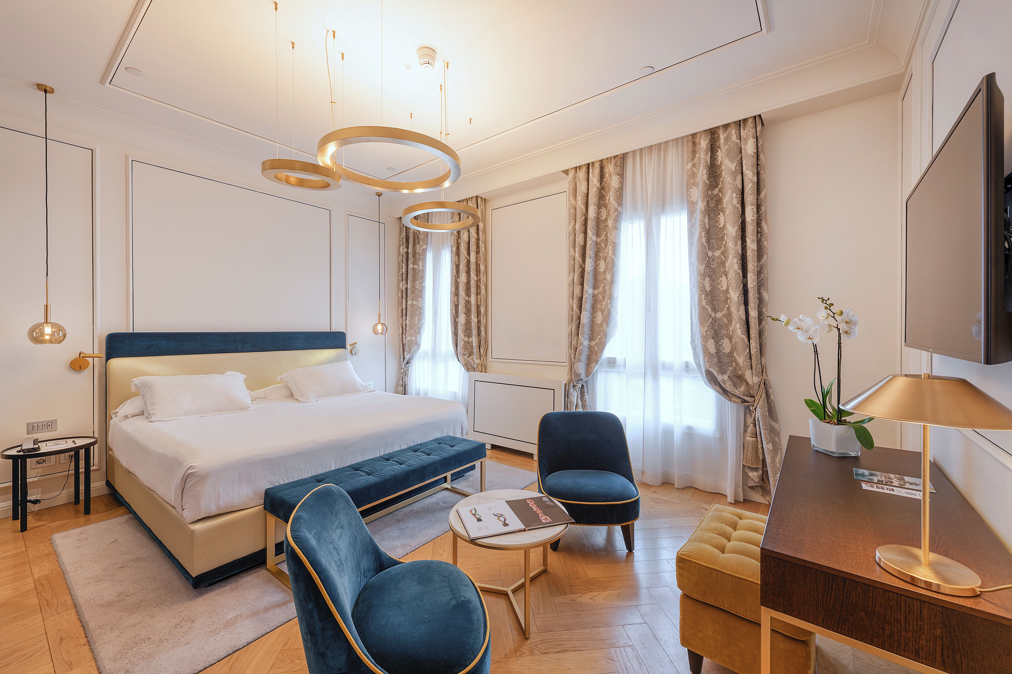Une chambre d’hôtel moderne avec un grand lit, deux fauteuils, une petite table, un bureau avec une lampe et un téléviseur.