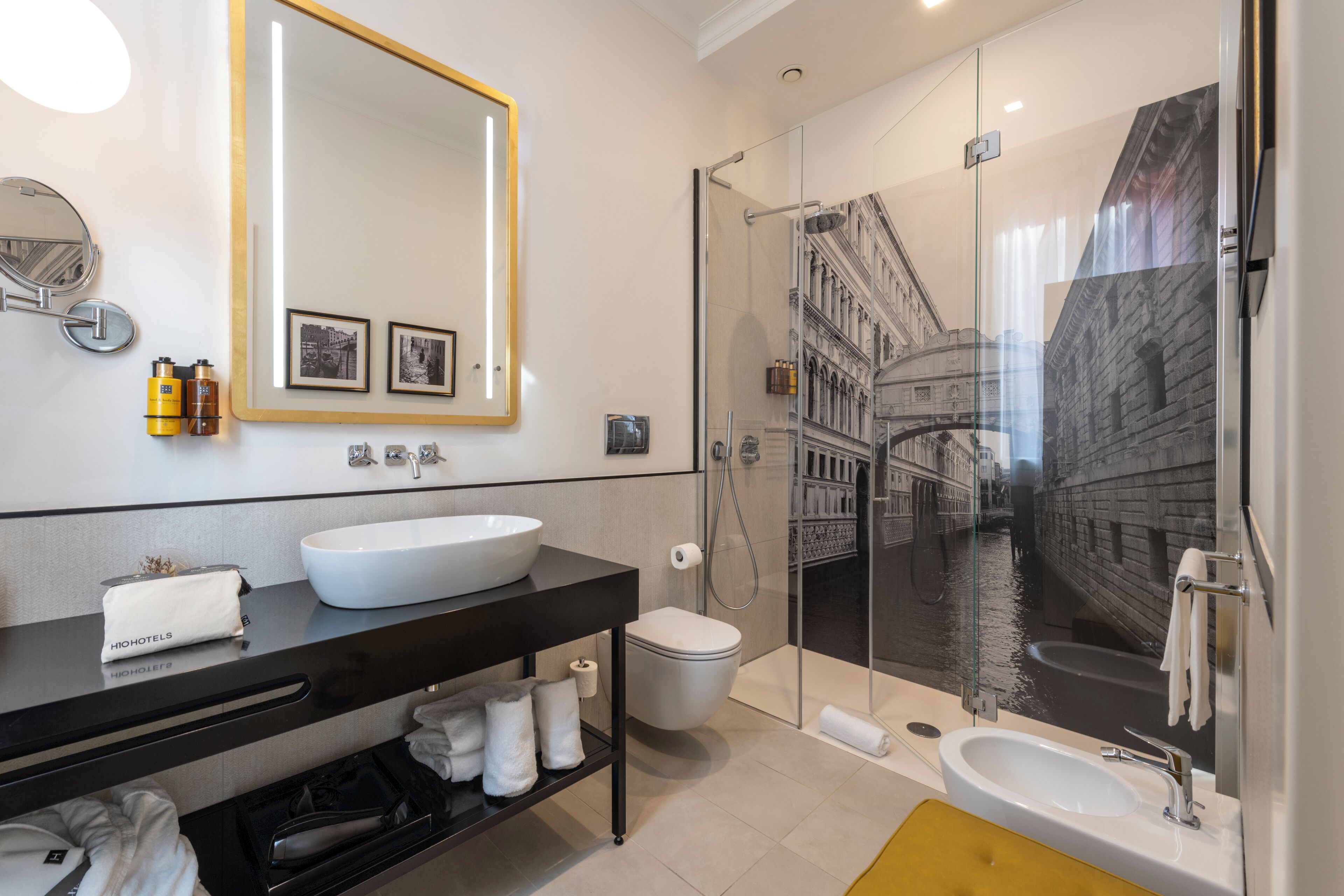 Un bagno moderno con uno specchio grande, un lavandino bianco, un water e una cabina doccia in vetro.