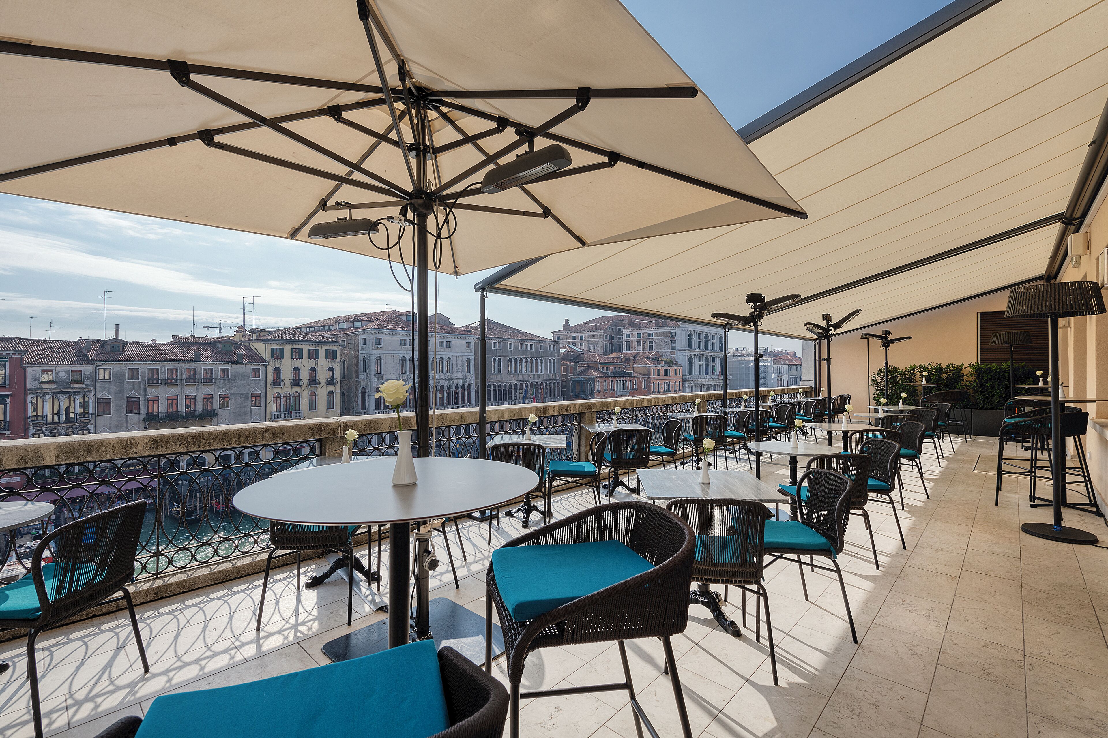 Una terraza con mesas y sillas, vista de la ciudad y una barandilla.