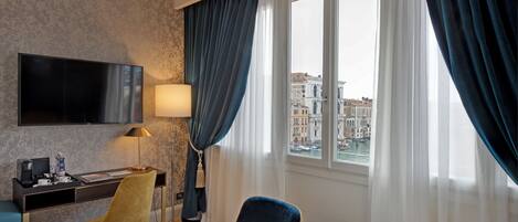 A hotel room with a bed, a desk with a flat-screen TV, a chair, a lamp, and a view of a cityscape through a window.