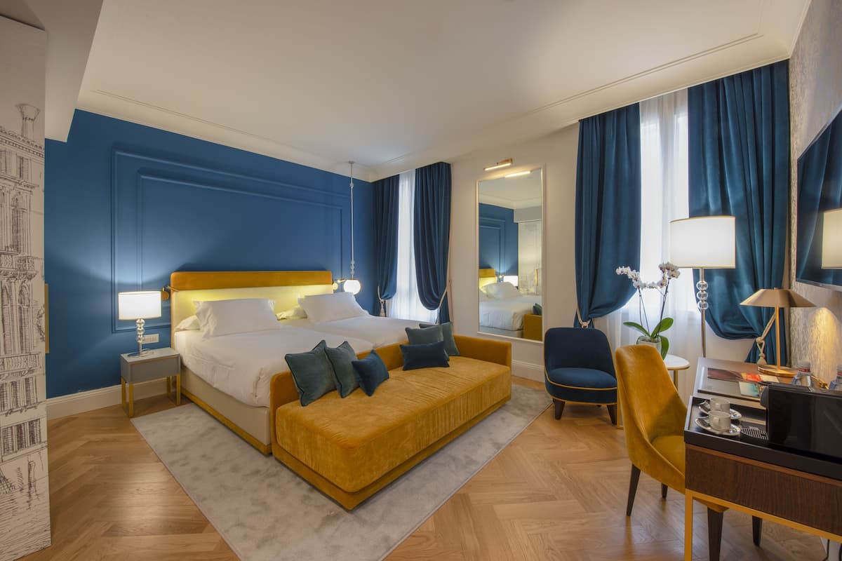 Una habitación de hotel con cama, sofá, escritorio, silla, espejo y ventana con cortinas.