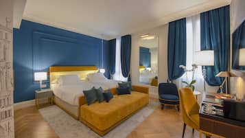 A hotel room with a bed, a sofa, a desk, a chair, a mirror, and a window with curtains.