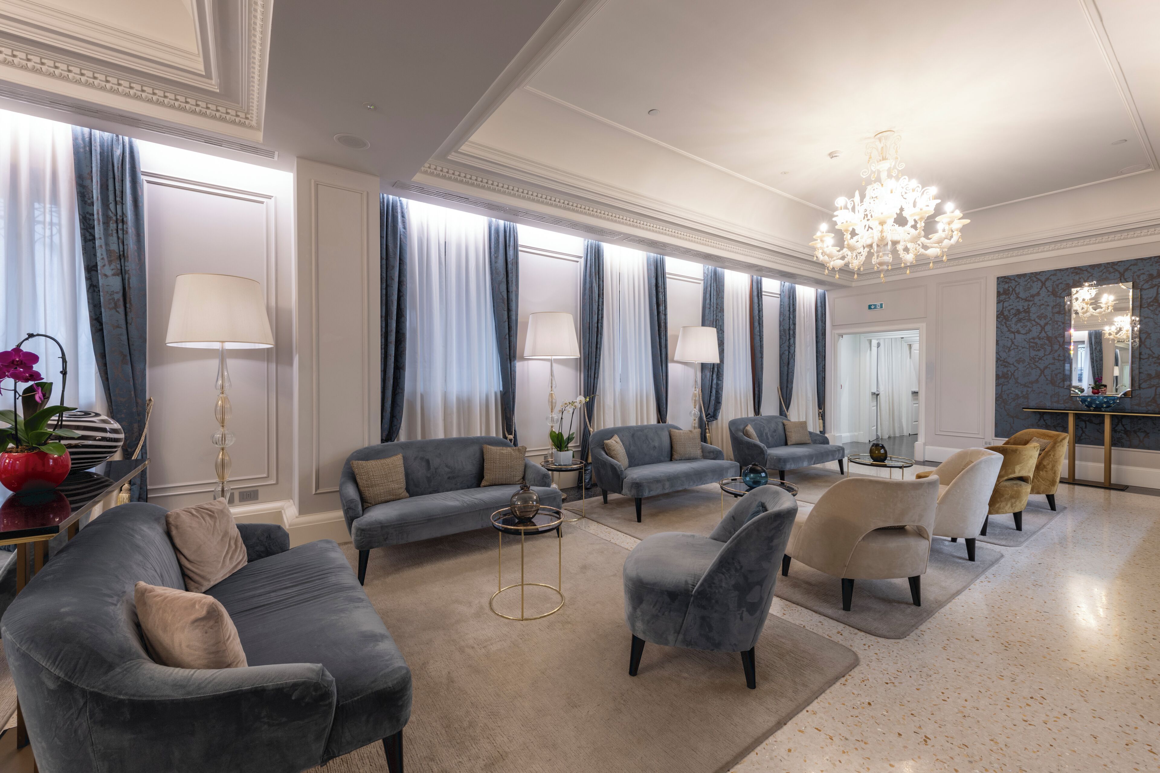 A spacious living room with a chandelier, grey sofas, armchairs, and a coffee table.
