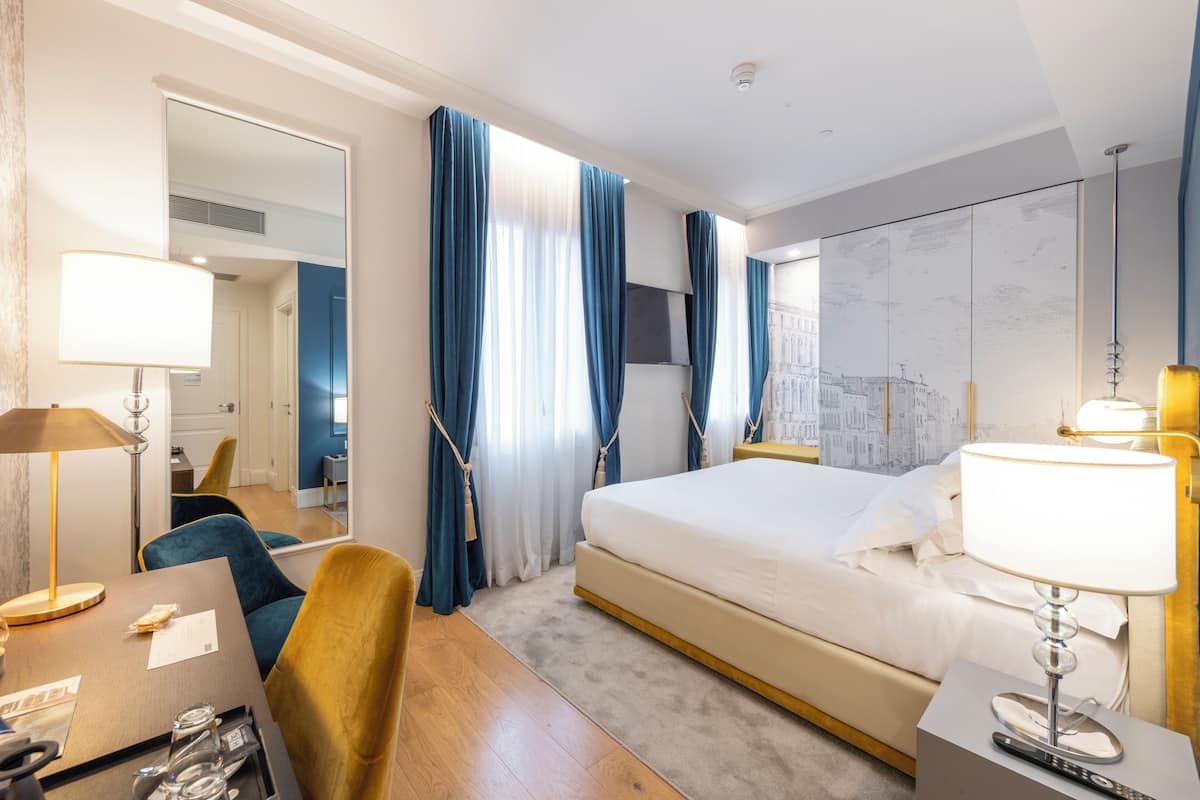 Una habitación de hotel con cama, escritorio, silla, lámpara y espejo.
