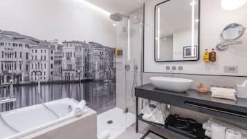 Un baño moderno con una bañera grande, una ducha con mampara de cristal, un espejo amplio y un lavamanos instalado en la pared.
