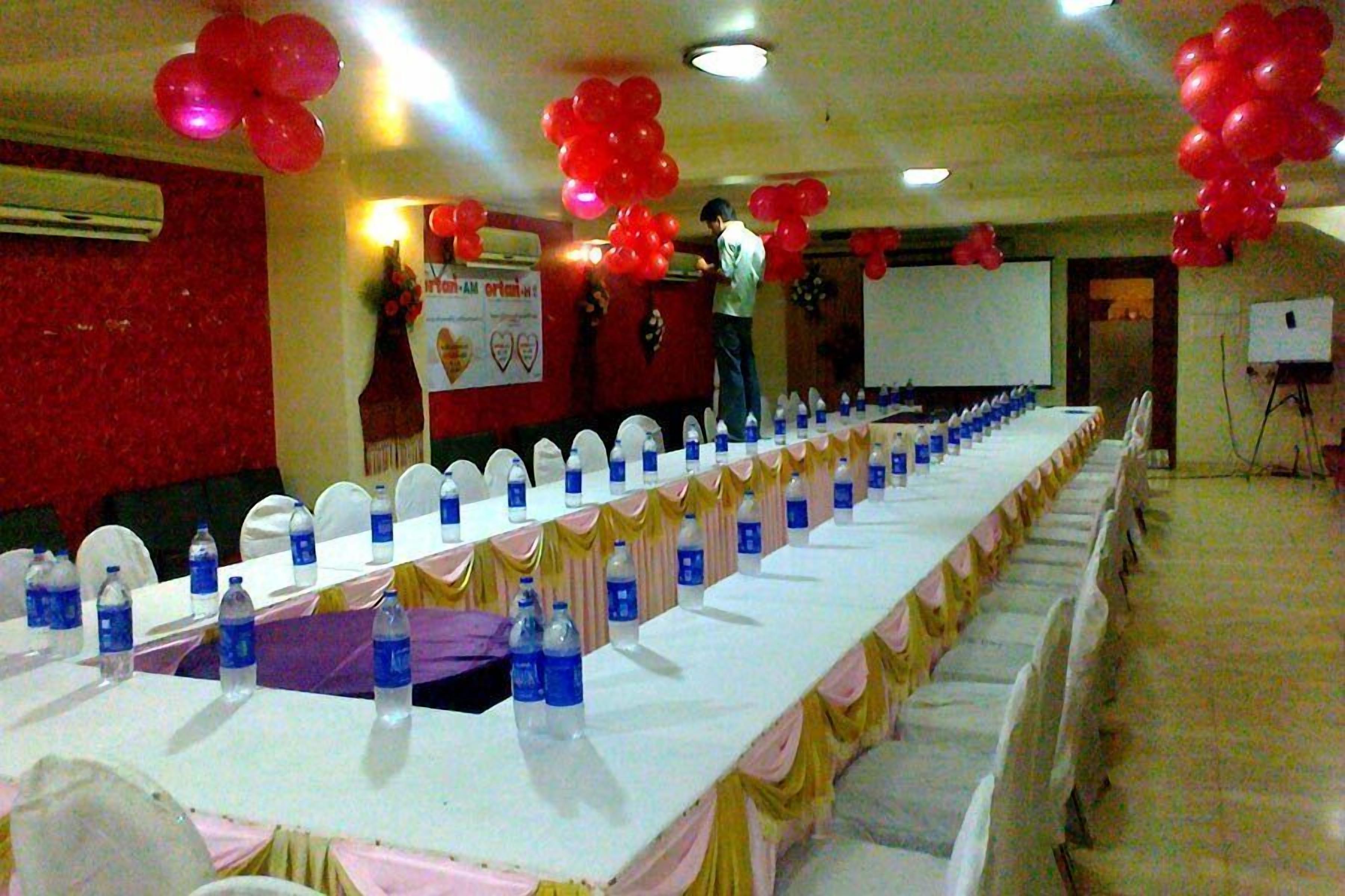 A conference room with a long table set for a meeting, balloons, and a projector screen.