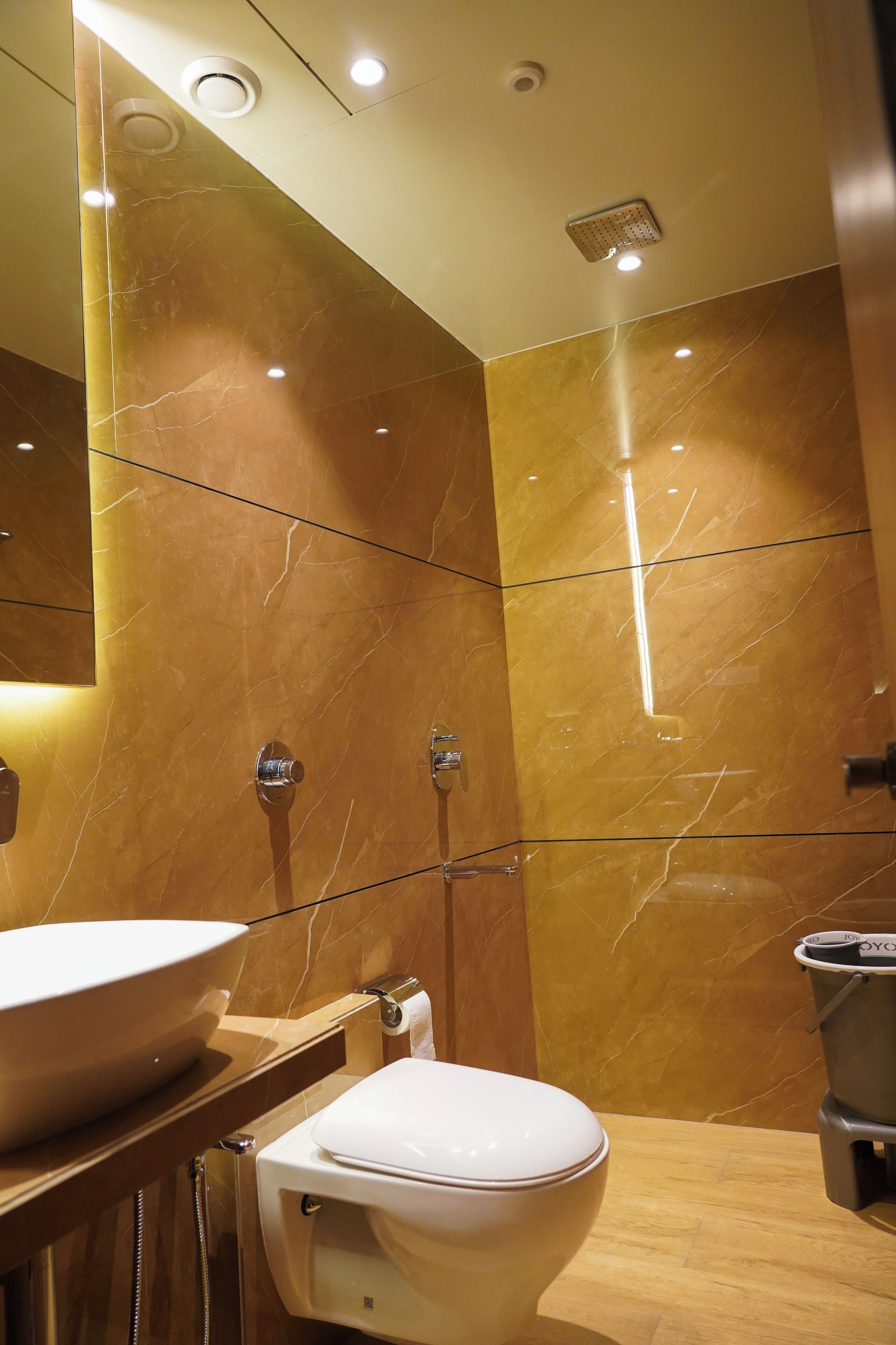 A modern bathroom with a marble wall, a large sink, a toilet, and a shower area.