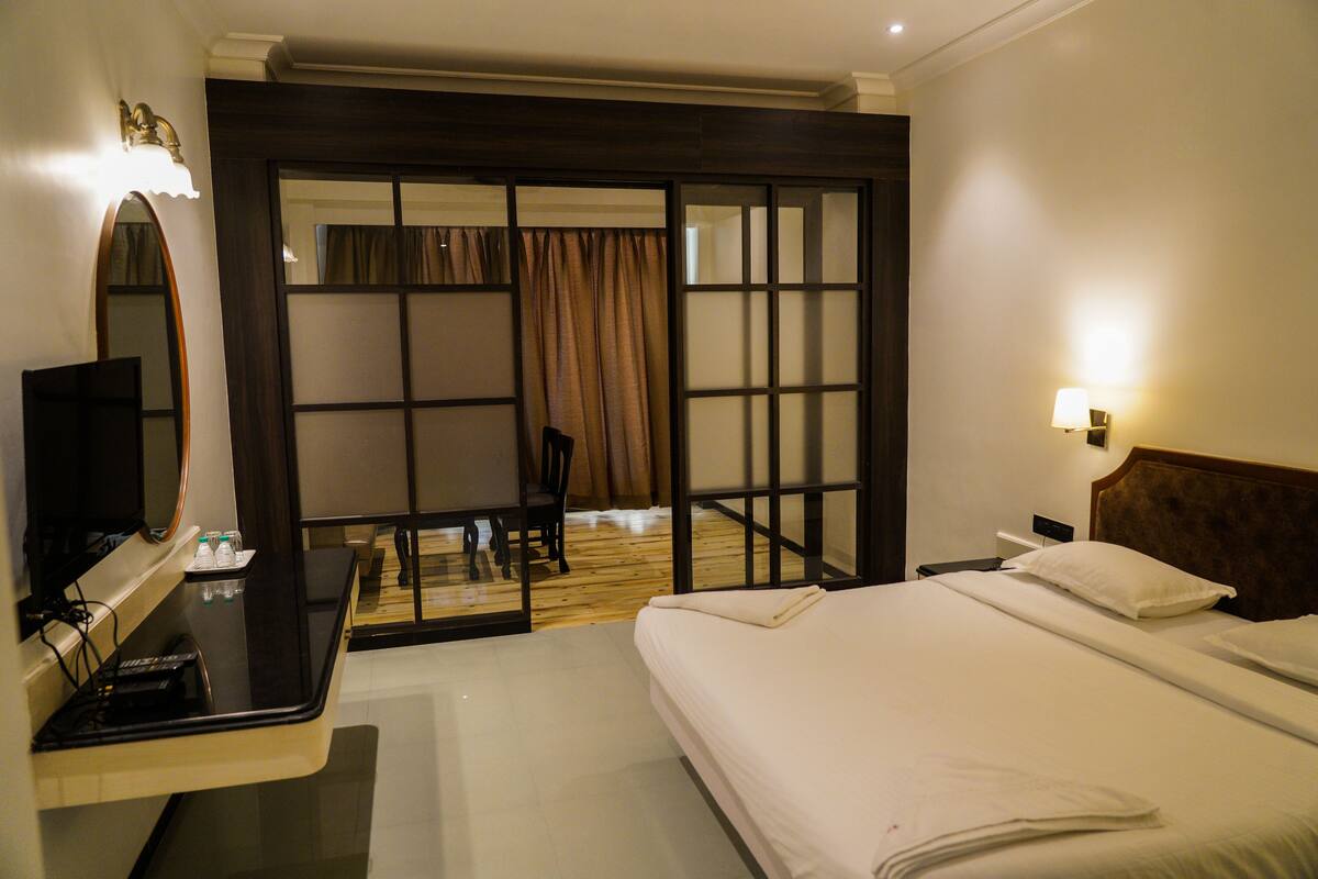 A hotel room with a bed, a desk with a mirror, a chair, and a sliding door leading to a balcony.