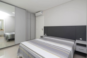 Ein modernes Schlafzimmer mit einem großen Bett, einem Kleiderschrank, einem Nachttisch und einer Klimaanlage.