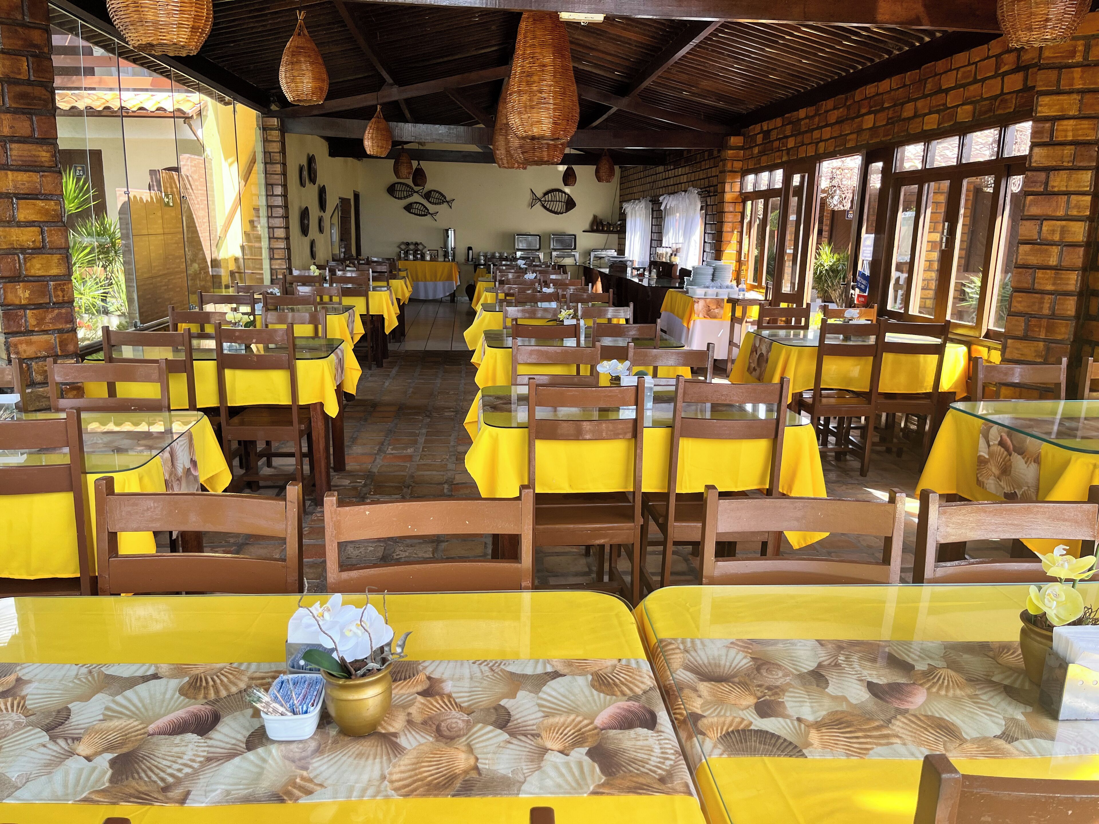 Un restaurante con manteles amarillos, sillas de madera y una pared de ladrillo.