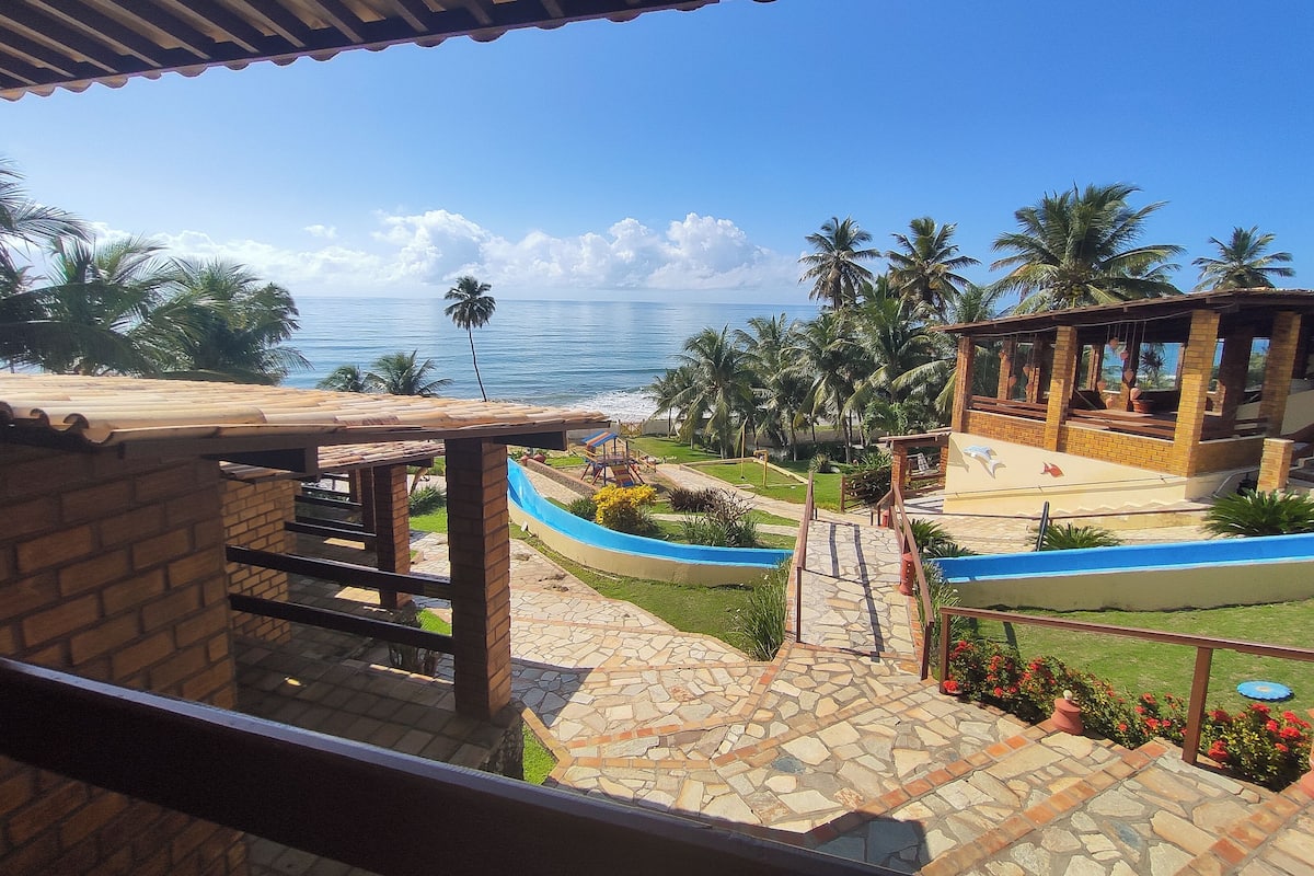 A view from a balcony overlooking a pool area with a beach and palm trees.