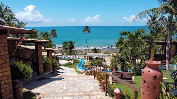 Un resort con un camino de piedra que conduce a una playa, palmeras y una vista despejada del océano.