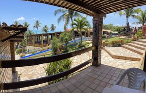 A covered outdoor area with a pool, palm trees, and a view of the ocean. - Pousada Enseada do Sol (Conde)