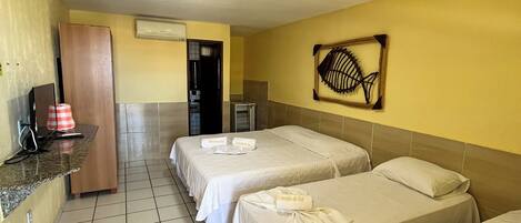 A hotel room with three beds, a small desk, a mirror, and a wall-mounted artwork.