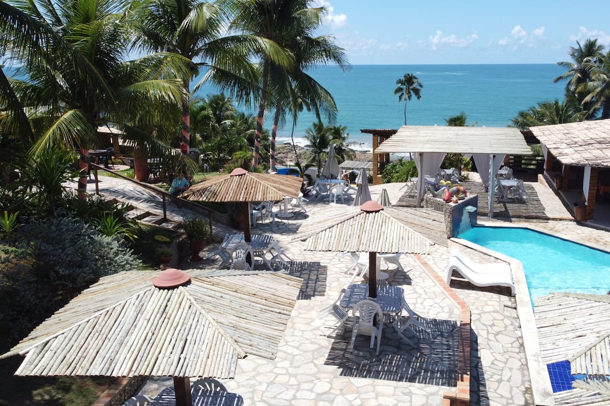 A pool area with umbrellas, lounge chairs, and a view of the ocean.