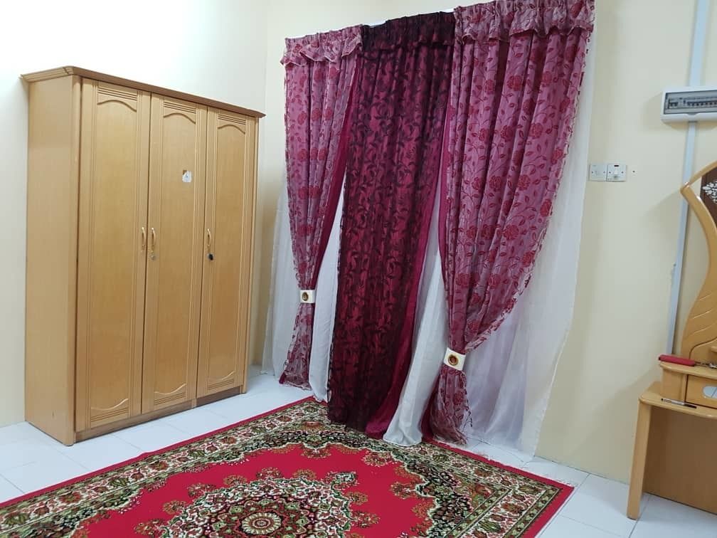 A room with a wooden wardrobe, a patterned red carpet, and a curtain with a floral design.