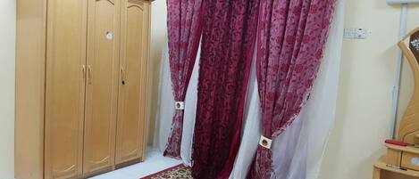 A room with a wooden wardrobe, a patterned red carpet, and a curtain with a floral design.