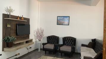 Un soggiorno con televisore, due poltrone in pelle, un divano, un mobile TV in legno e un quadro appeso al muro.