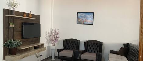 A living room with a TV, two leather armchairs, a sofa, a wooden TV stand, and a painting on the wall.