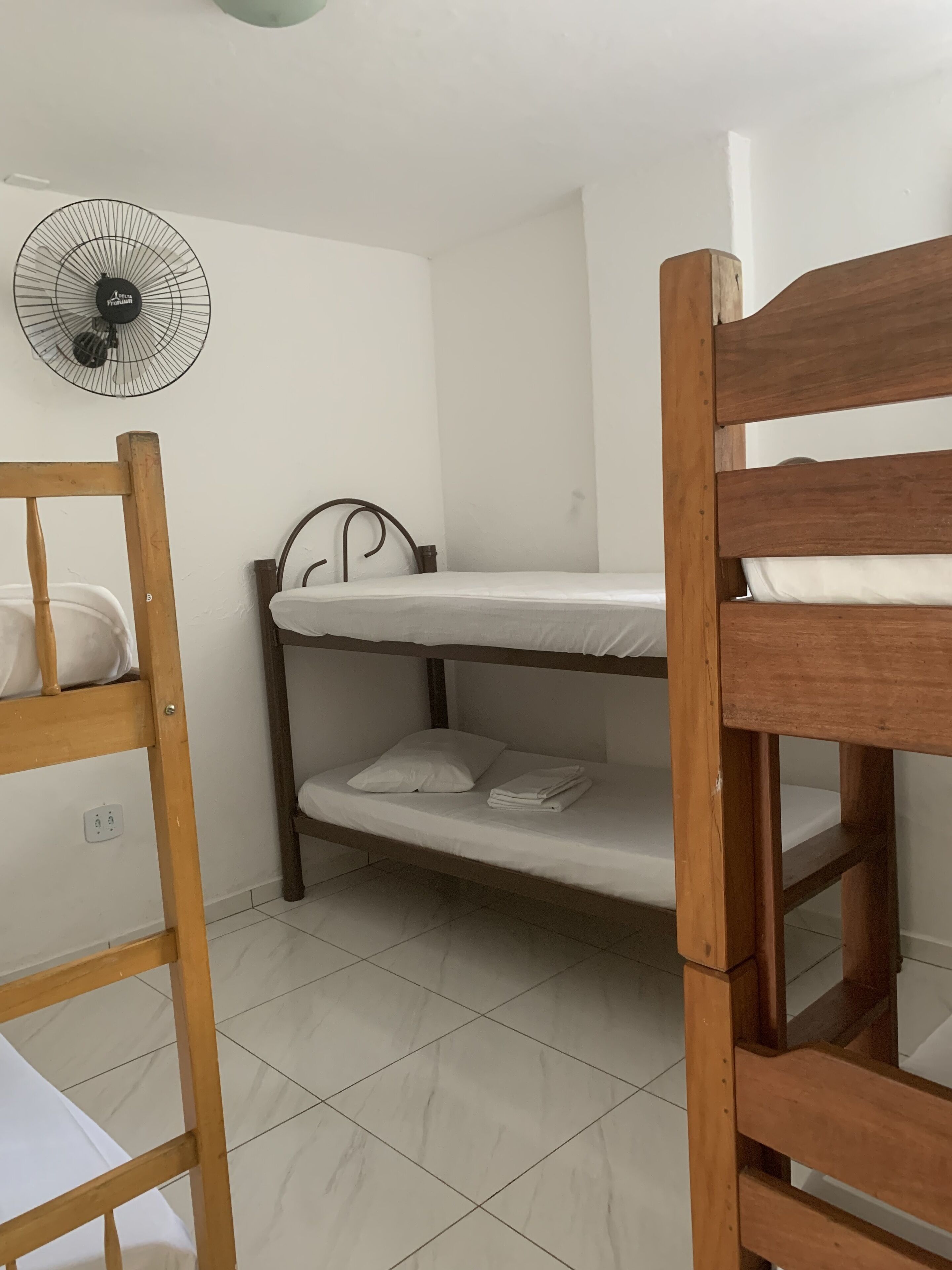 A bunk bed room with a ceiling fan, white walls, and tiled flooring.