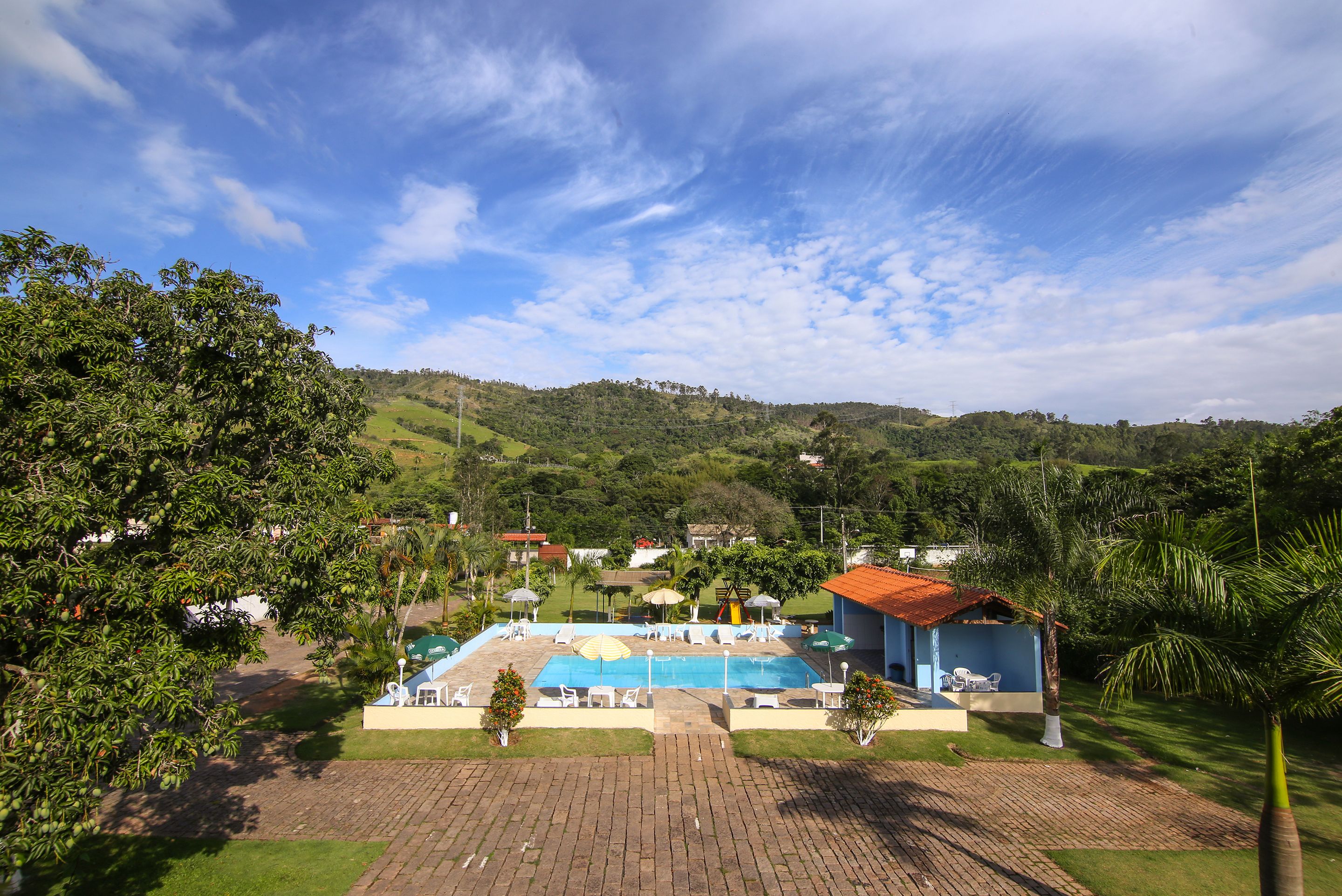 A pool area with lounge chairs and umbrellas, surrounded by greenery and hills.