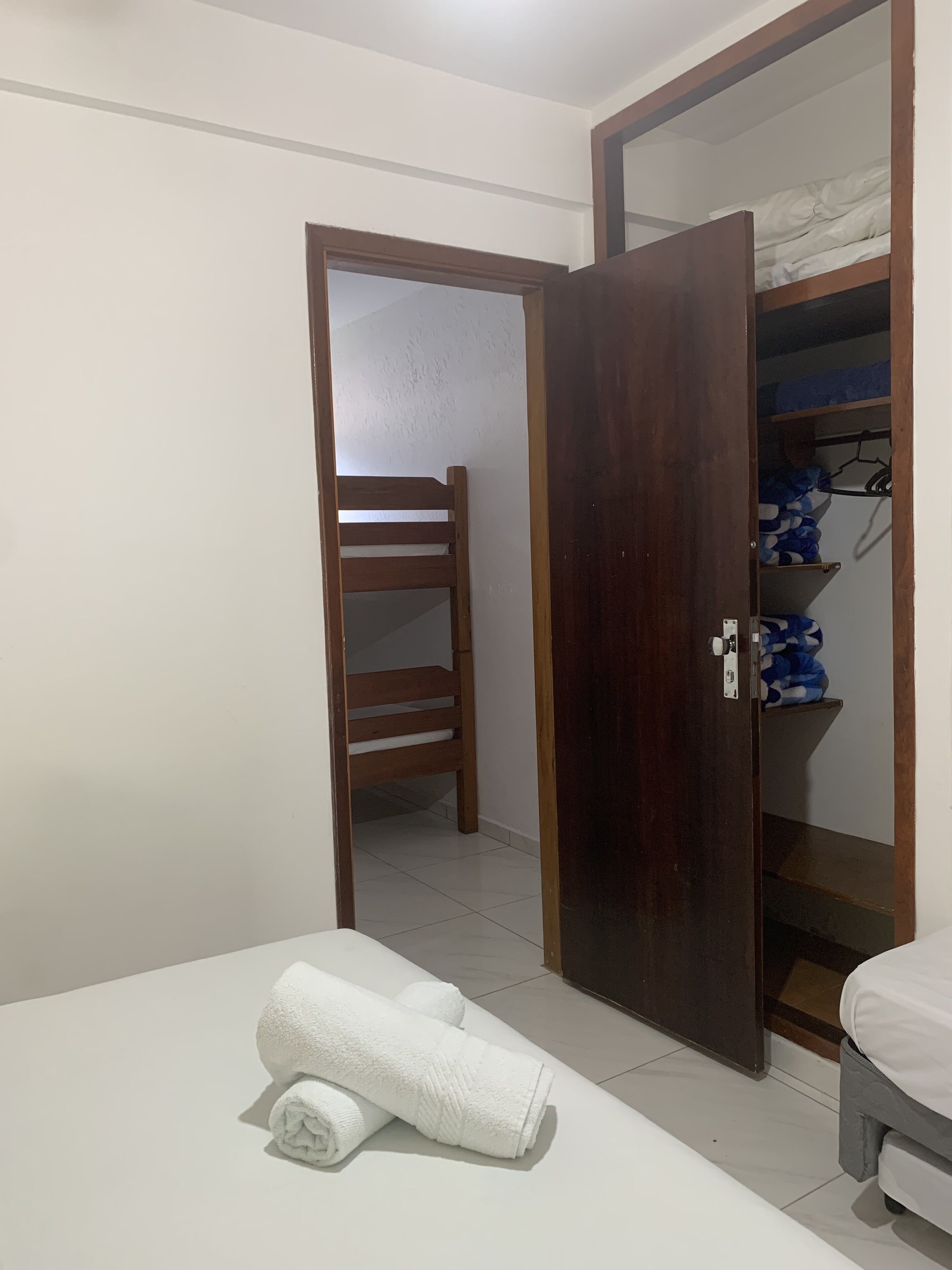 Una habitación con una cama, una silla de madera, un armario y una puerta que da a otra estancia.