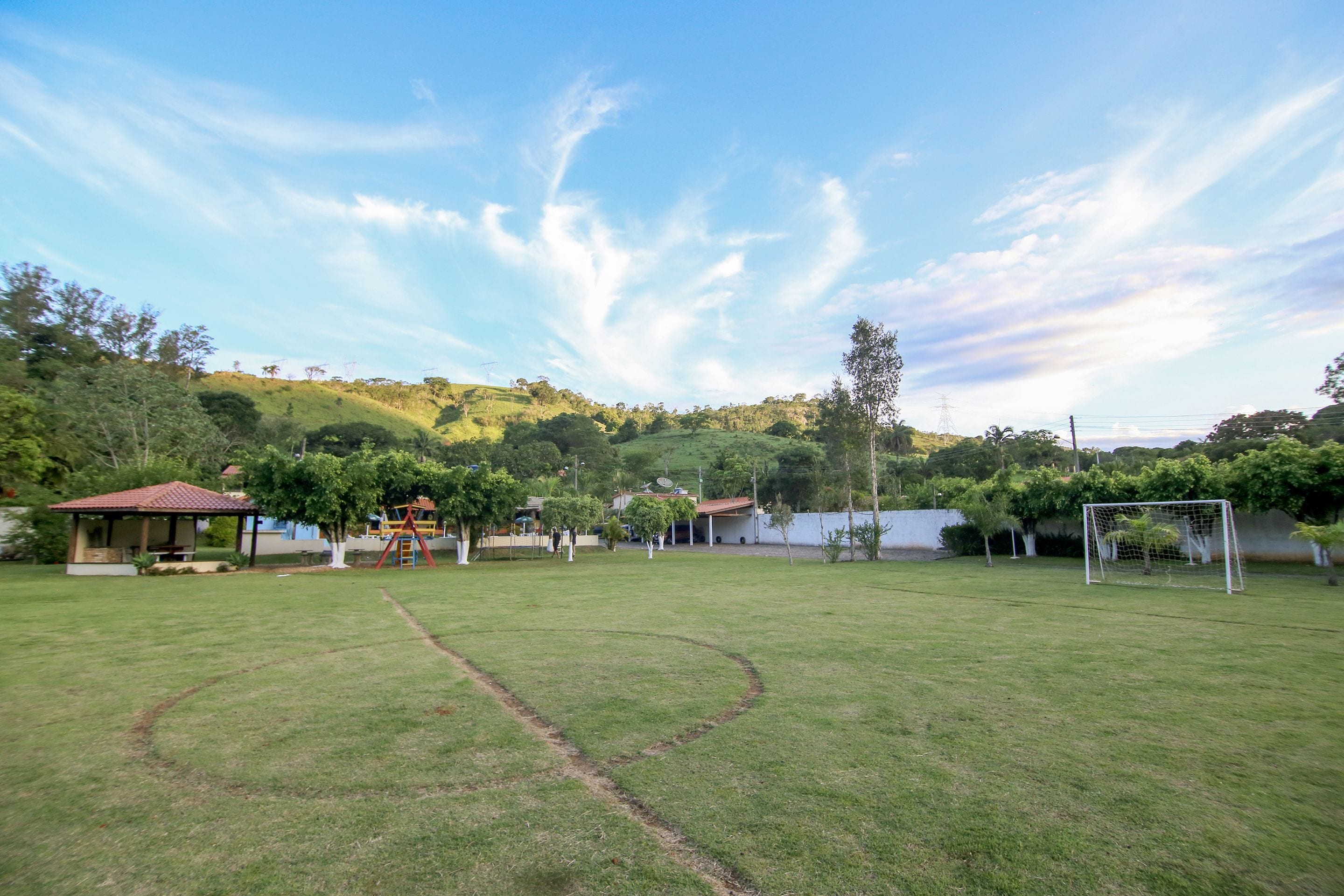 Un campo cubierto de césped con un arco de fútbol, un pequeño pabellón y un parque infantil.