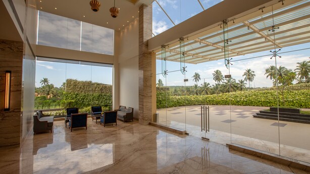 A spacious lobby with a high ceiling, large windows, and a view of palm trees. - Nanu Resort, Arambol (Arambol)