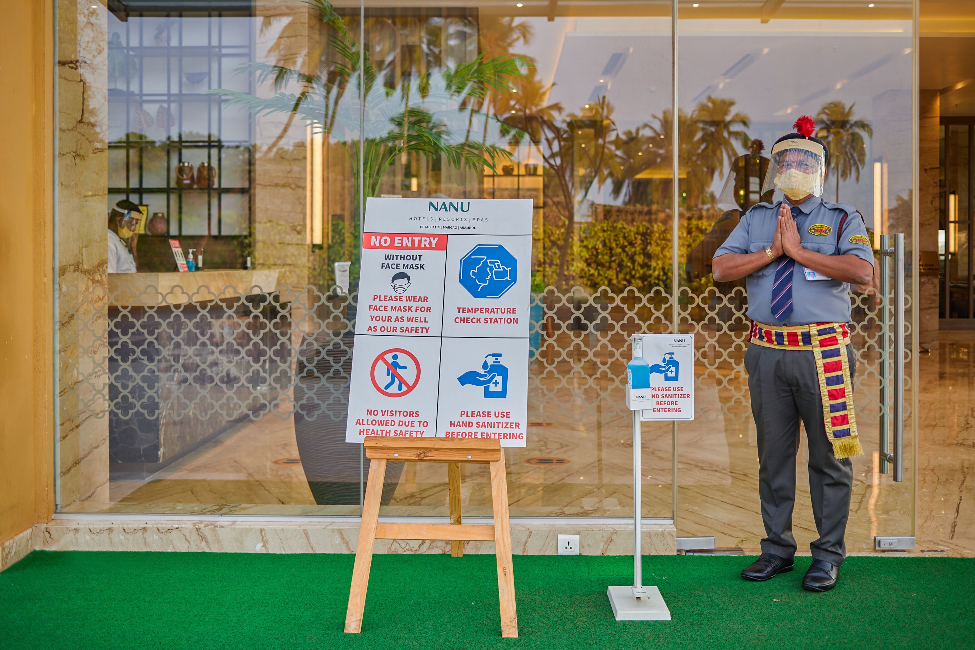 A security guard standing in front of a hotel entrance with a signboard displaying health and safety guidelines.