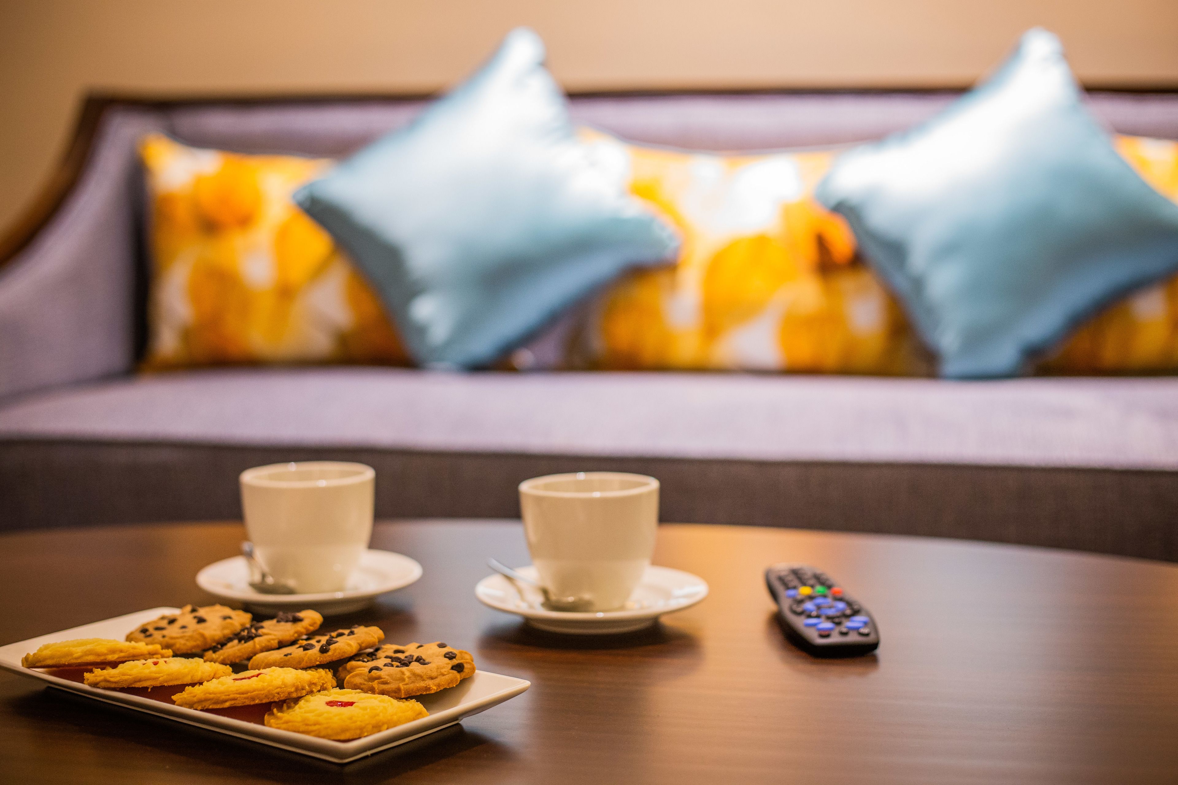 A dining table with a plate of cookies, two cups of coffee, and a remote control.