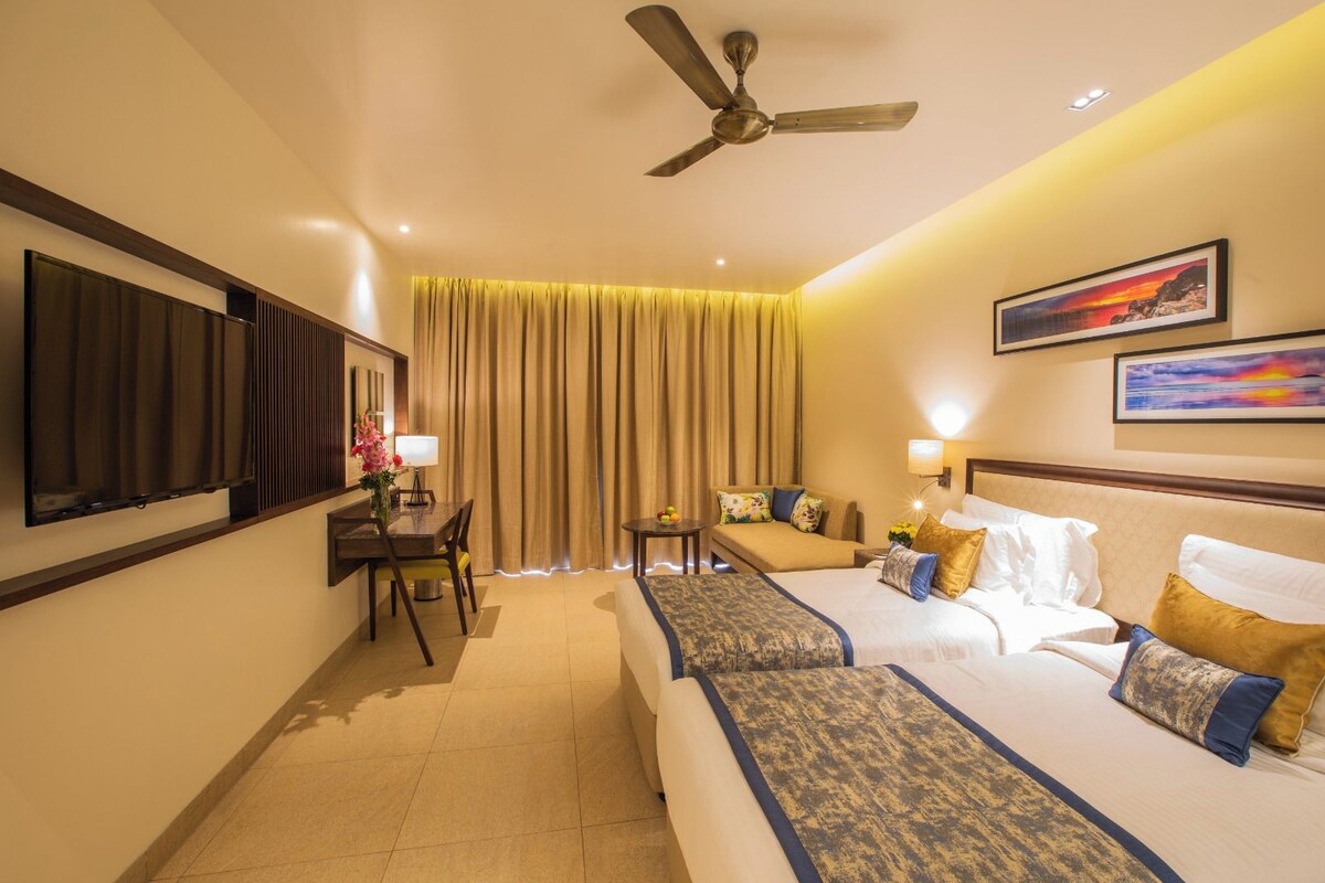 A hotel room with a bed, a sofa, a desk, a chair, a ceiling fan, and a large window with curtains.
