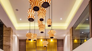 A modern lobby with a marble reception desk, decorative hanging lamps, and a large wooden panel wall. - Nanu Resort, Arambol (Arambol)