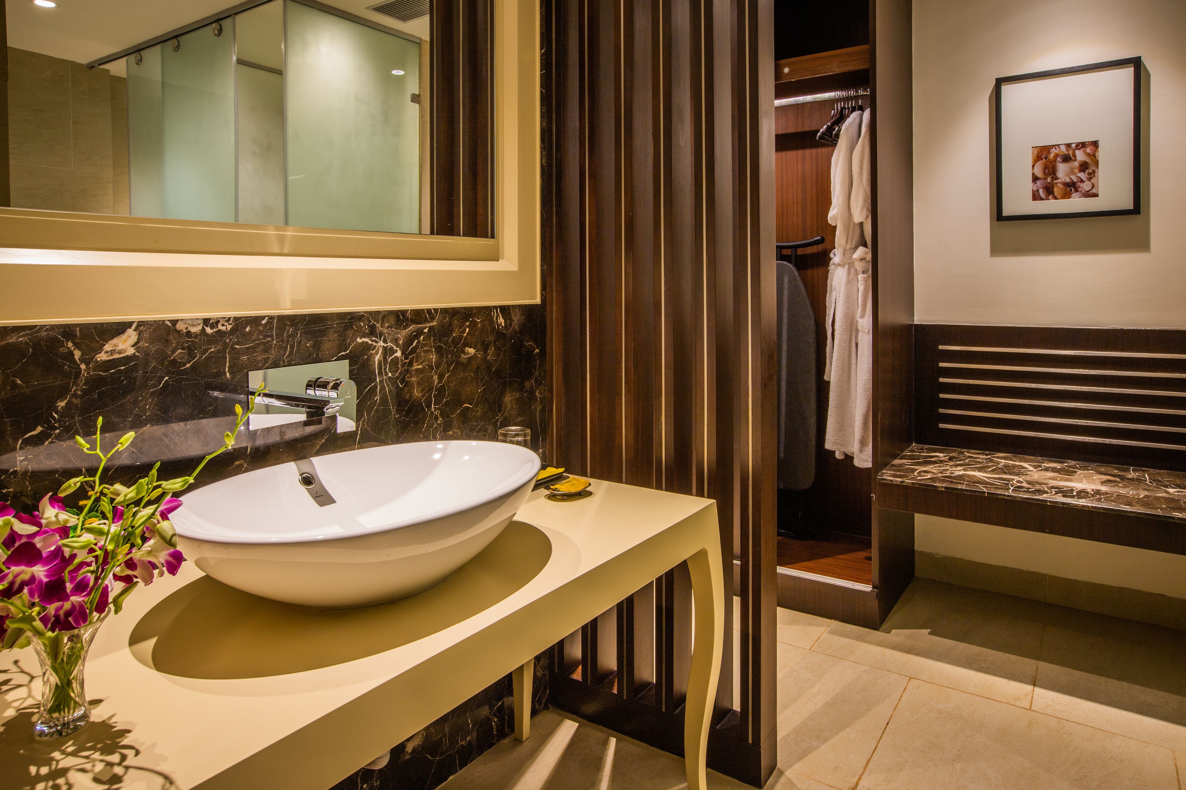 Une salle de bain moderne avec un grand lavabo blanc, un miroir et un vase de fleurs.
