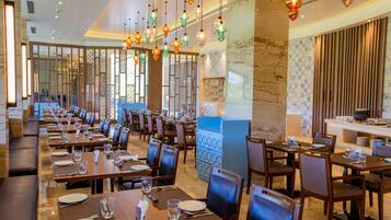 Un comedor amplio con varias mesas y sillas, lámparas decorativas colgantes y vistas al área de la cocina.