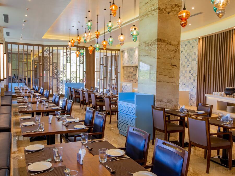 Un comedor amplio con varias mesas y sillas, lámparas decorativas colgantes y vistas al área de la cocina.