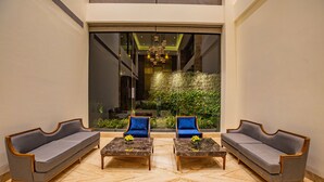 A lobby with two sofas and two matching armchairs, a marble floor, and a large window with a view of greenery and a building interior. - Nanu Resort, Arambol (Arambol)