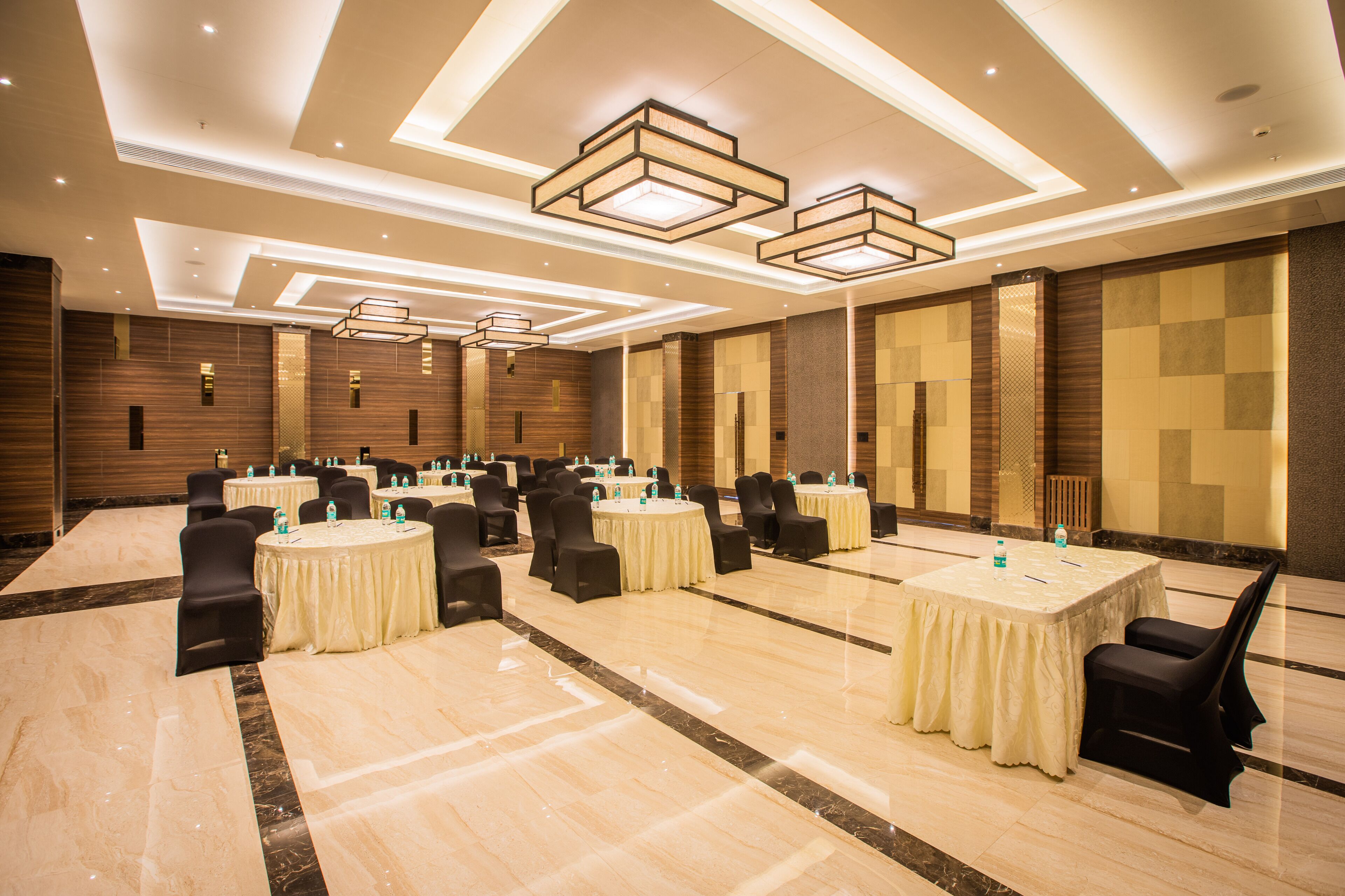 A spacious conference room with multiple tables and chairs, equipped with water bottles and pens, and features a modern ceiling design with recessed lighting.