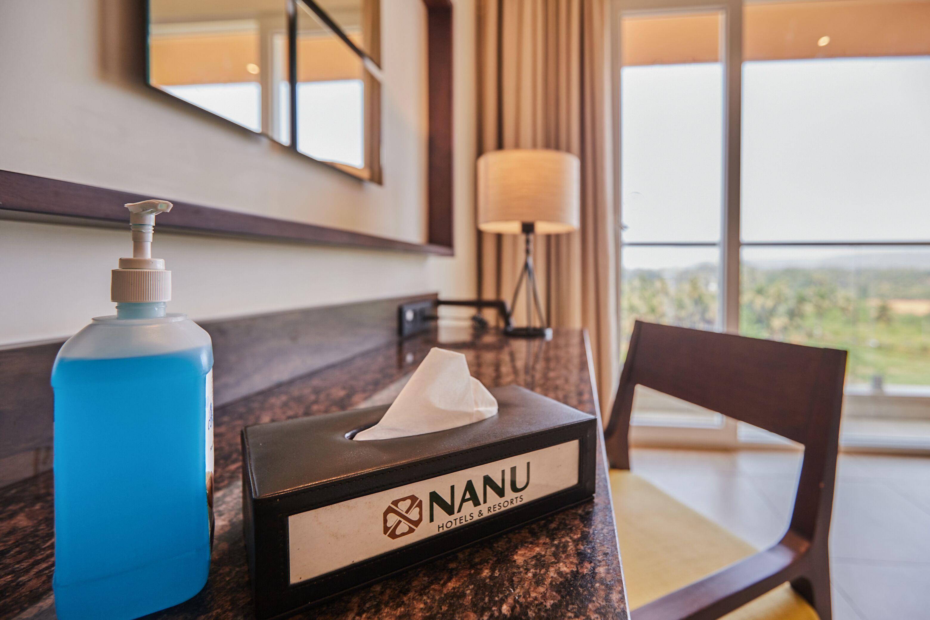 A hotel room with a bathroom counter featuring a blue bottle, a tissue box, and a chair.