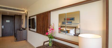 A hotel lobby with a reception desk, a vase of flowers, a large mirror, and a lamp.