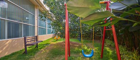 A playground with a swing set and a bench, surrounded by grass and plants.