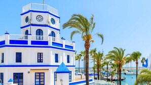 A white building with blue accents and a clock tower, surrounded by palm trees and boats. - Hotel Mare Estepona (Estepona)